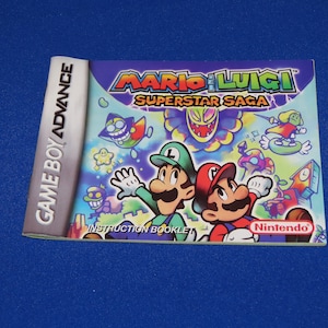 May include: A colorful Game Boy Advance instruction booklet for the game Mario & Luigi: Superstar Saga. The cover features Mario and Luigi in a cartoon style, along with other characters from the game.