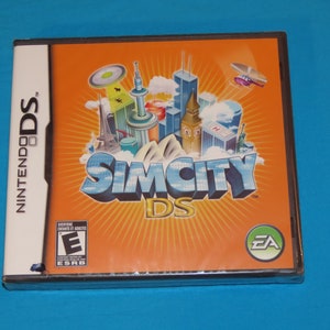 May include: A Nintendo DS game case with an orange background and a cityscape illustration. The game title is "SimCity DS" with the EA logo in the bottom right corner. The ESRB rating is "E for Everyone".