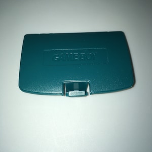 May include: A teal green Game Boy Color game cartridge case with the word "GAME BOY" embossed on the front.