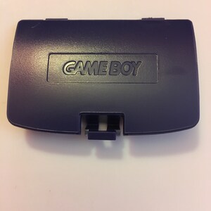 May include: A dark purple Game Boy cartridge case with the words "GAME BOY" printed in white on the front.