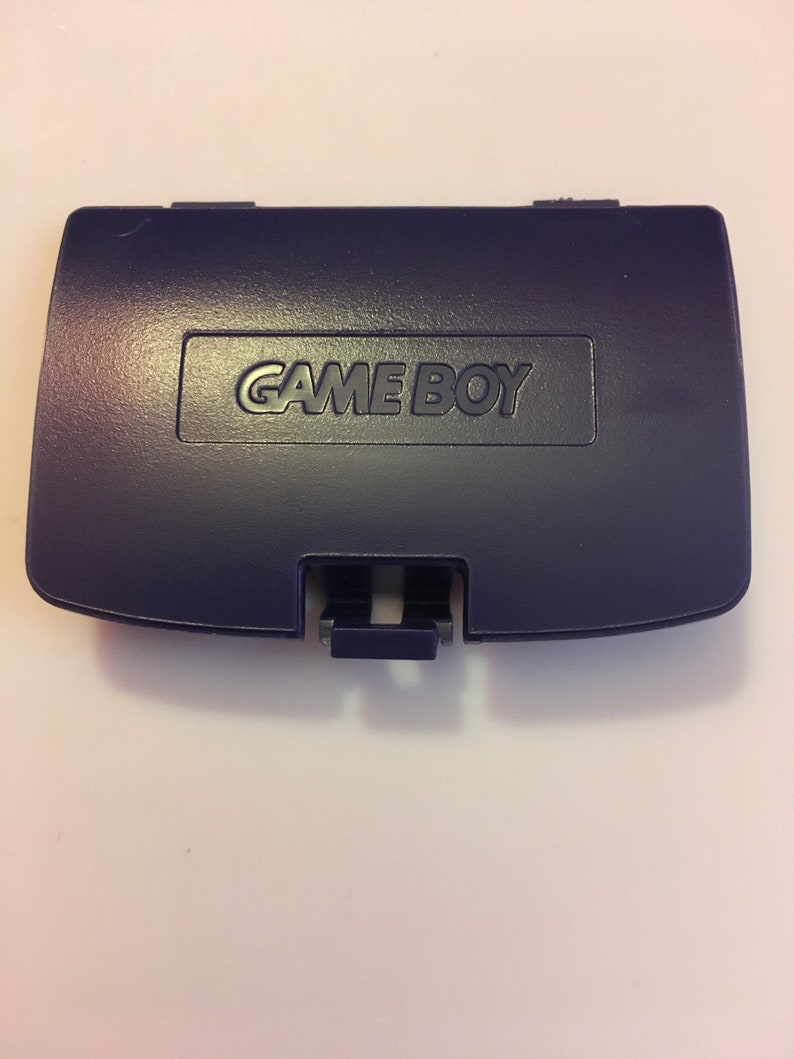 May include: A dark purple Game Boy cartridge case with the words "GAME BOY" printed in white on the front.