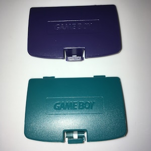 May include: Two Game Boy Color game cartridge covers. One is purple and the other is teal.