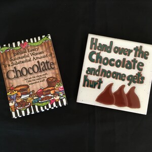 May include: Two decorative tiles with a chocolate theme. One tile features a book with the text "Behind Every Successful Woman Is a Substantial Amount of Chocolate" and a colorful illustration of chocolate desserts. The other tile features the text "Hand over the Chocolate and no one gets hurt" with three chocolate kisses.