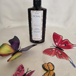 May include: A black bottle of Jafra Royal Almond body oil with a pump dispenser, next to four colorful butterfly decorations. The bottle contains 225 ml / 7.6 fl oz of body oil.