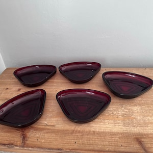 Op de afbeelding: Vijf kleine, driehoekige, robijnrode glazen schalen op een houten oppervlak.