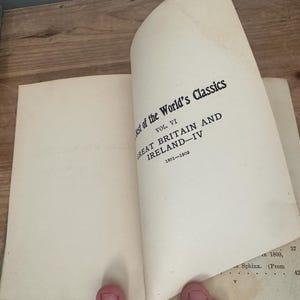 May include: An open book with the title "Best of the World's Classics, Vol. VI, Great Britain and Ireland - IV, 1801-1909" printed in black on the right page. The book's pages are off-white, and the background is a wooden surface.