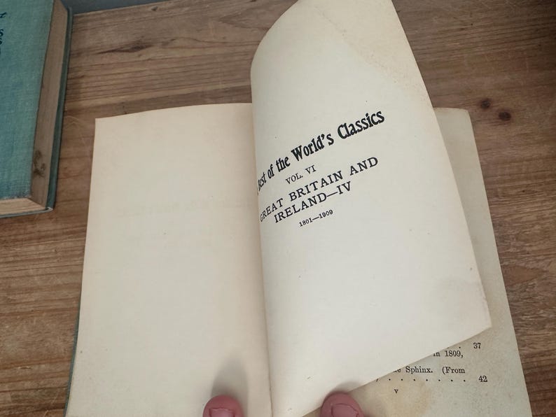 May include: An open book with the title "Best of the World's Classics, Vol. VI, Great Britain and Ireland - IV, 1801-1909" printed in black on the right page. The book's pages are off-white, and the background is a wooden surface.