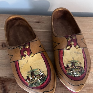 May include: Pair of wooden clogs painted with a scene of a windmill and the word "Diest". The clogs are brown with red and gold accents.