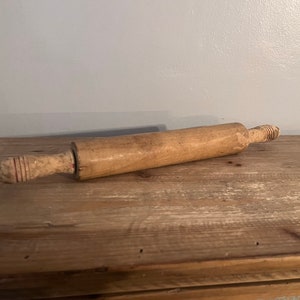 Può includere: Un mattarello di legno con dettagli dipinti in rosso e bianco. Il mattarello è appoggiato su una superficie di legno.
