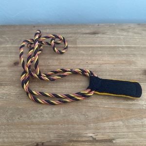 May include: A black, yellow, and pink braided cord with a black fabric loop at the end.