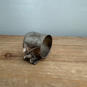 Könnte beinhalten: Ein silberner Serviettenring mit Vogelmotiv. Der Ring ist aus Metall und hat eine glatte, polierte Oberfläche.