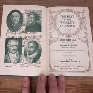 May include: Open book titled "The Best of the World's Classics" featuring portraits of Taine, Dante, Goethe, and Cervantes. The book is open to a page with text and decorative borders. The book is on a wooden surface.