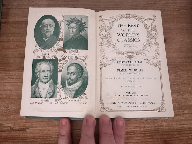 May include: Open book titled "The Best of the World's Classics" featuring portraits of Taine, Dante, Goethe, and Cervantes. The book is open to a page with text and decorative borders. The book is on a wooden surface.