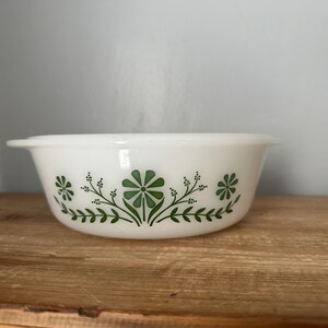 Peut inclure: Plat à four en céramique blanche avec un motif floral vert. Le plat a une forme arrondie et un bord légèrement évasé.