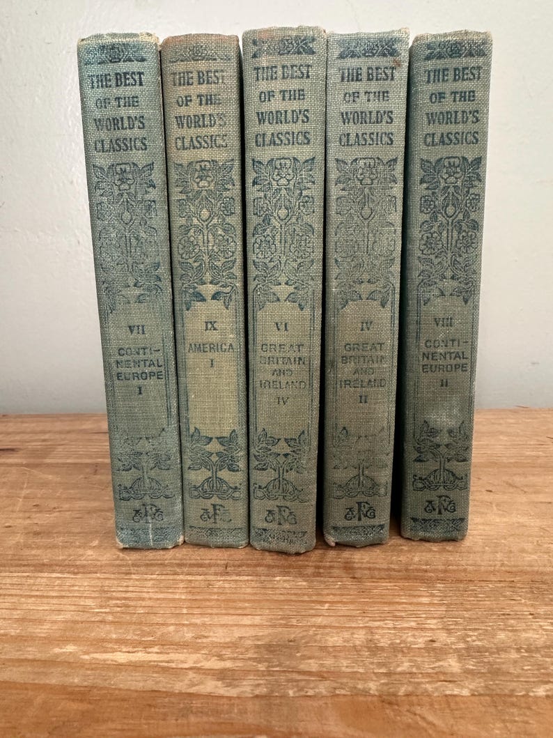 May include: A collection of five antique books titled "The Best of the World's Classics." The books have light blue covers with ornate floral designs and text. The spines display the title and volume numbers, including "America" and "Continental Europe."