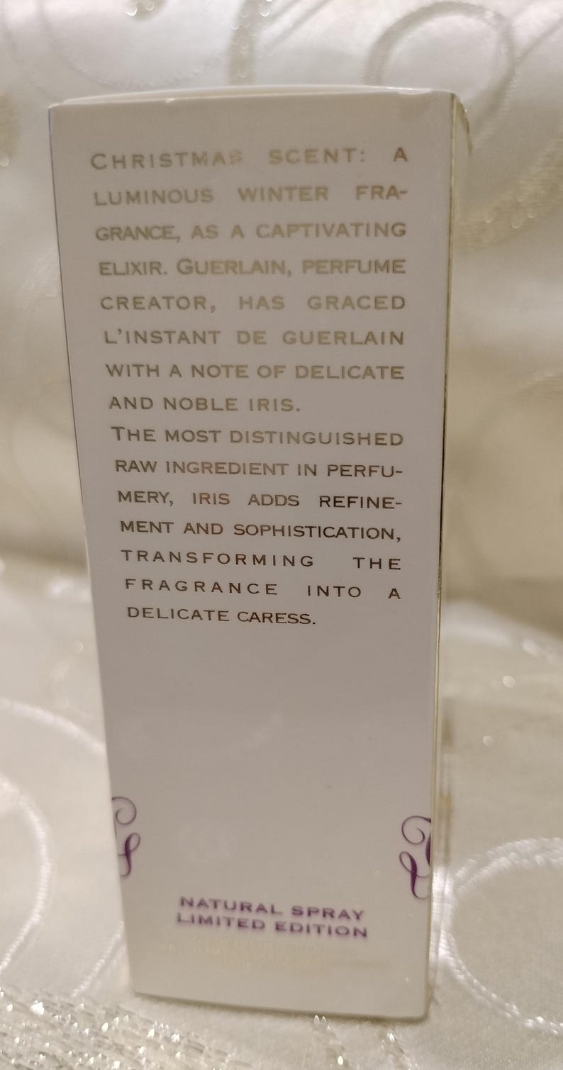 May include: A white perfume box with text describing a luminous winter fragrance. The text includes phrases like "Christmas Scent," "delicate caress," and "noble iris." The box is a limited edition natural spray.