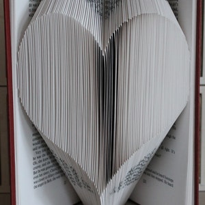 Peut inclure: Un livre blanc plié en forme de cœur. Le livre est ouvert et les pages sont pliées pour créer la forme du cœur. Le livre est posé sur une surface blanche.