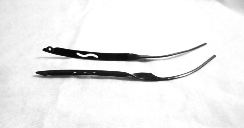 May include: Two black metal hair clips. One clip has a curved design and the other is straight.