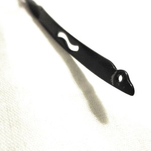 May include: A black metal wire with a small hole and a wavy design. The wire is bent into a curved shape.