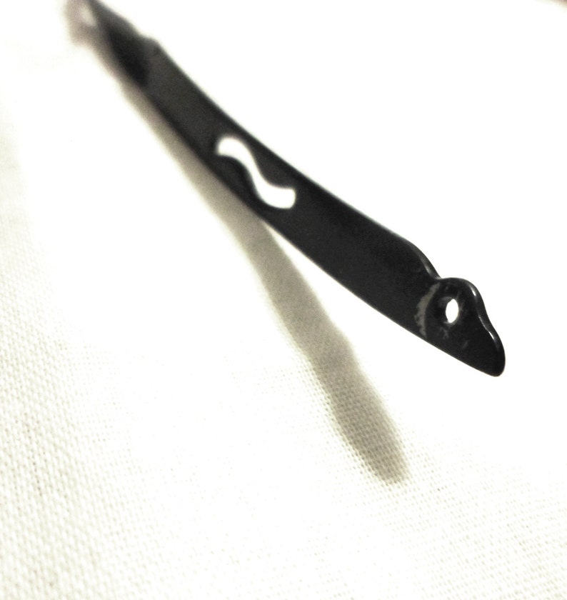 May include: A black metal wire with a small hole and a wavy design. The wire is bent into a curved shape.