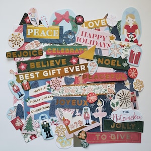 May include: A collection of Christmas-themed paper cutouts with various festive phrases like "Peace," "Happy Holidays," and "Noel." The cutouts feature snowflakes, nutcrackers, and gift illustrations in a mix of colors.