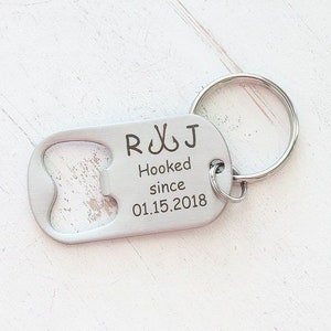 May include: A silver bottle opener keychain with the engraved text "R & J Hooked since 01.15.2018". The keychain has a bottle opener on one end and a keyring on the other.