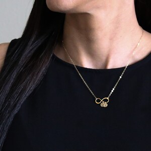 May include: A gold infinity necklace with two small round charms. The charms have letters on them.