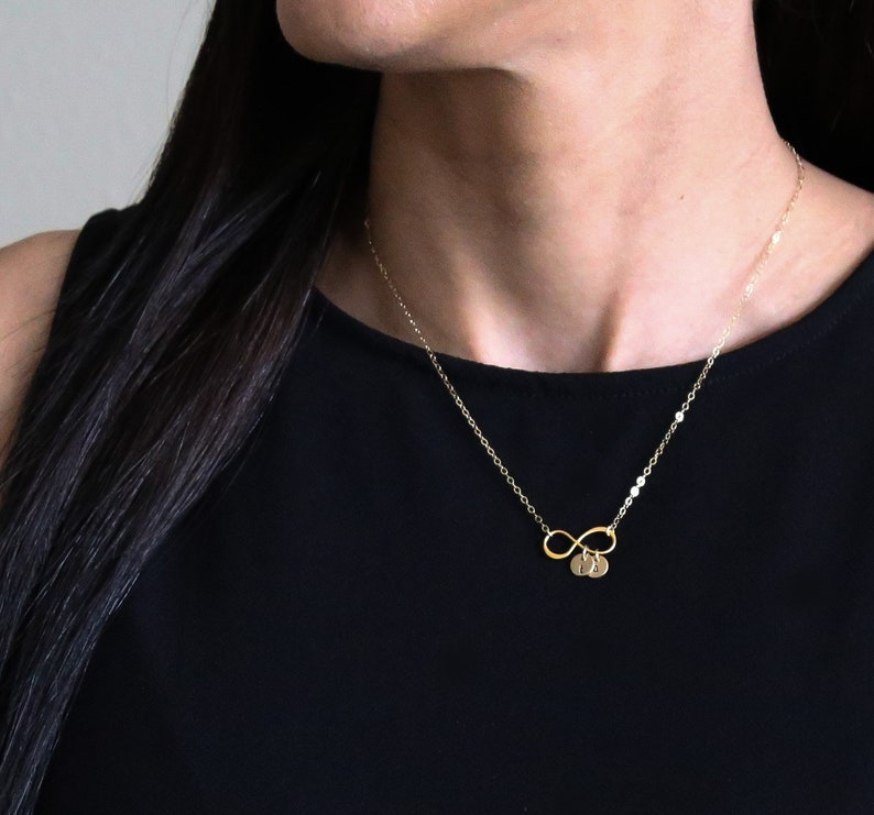 May include: A gold infinity necklace with two small round charms. The charms have letters on them.