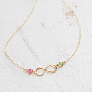 May include: A gold infinity necklace with a pink and green gemstone accent.