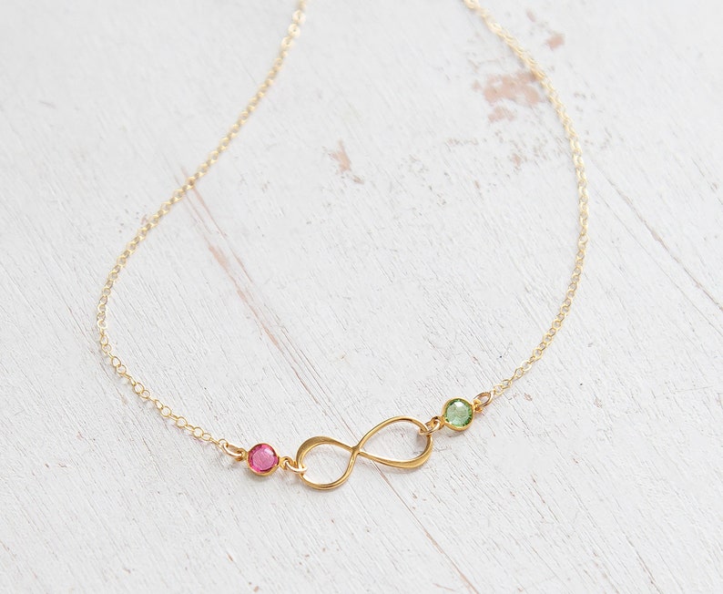 May include: A gold infinity necklace with a pink and green gemstone accent.