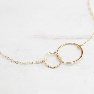 May include: A gold necklace with two interlocking circles. The circles are connected by a delicate chain.