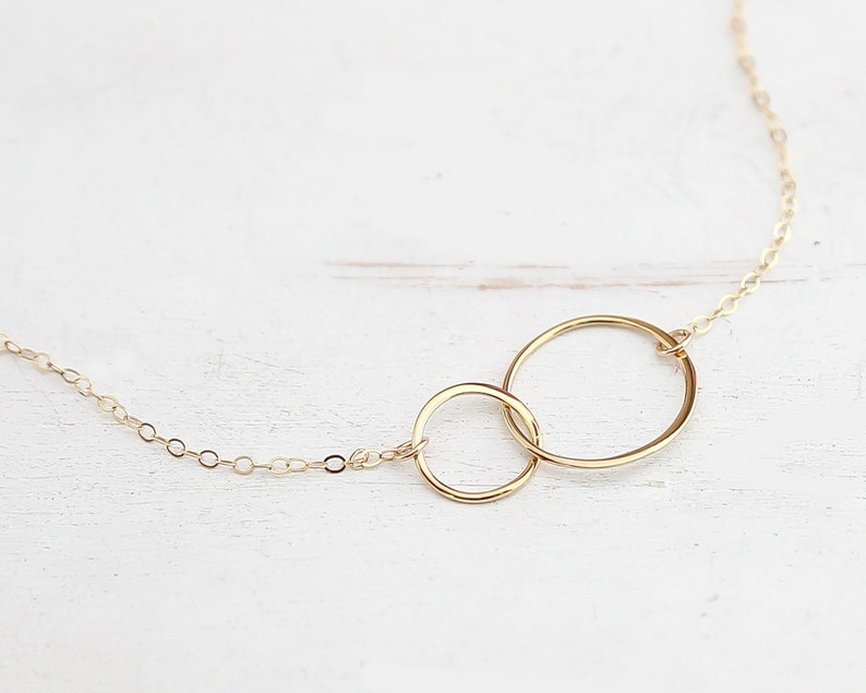 May include: A gold necklace with two interlocking circles. The circles are connected by a delicate chain.