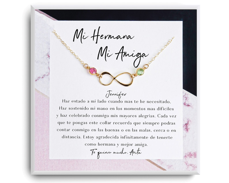 May include: A gold infinity necklace with pink and green gemstones. The necklace comes in a white box with a pink marble pattern and a message that reads "Mi Hermana Mi Amiga Jennifer Haz estado a mi lado cuando mas te he necesitado, Haz sostenido mi mano en los momentos mas dificiles y haz celebrado conmigo mis mayores alegrias. Cada vez que te pongas este collar recuerda que siempre podras contar conmigo en las buenas o en las malas, cerca o en distancia. Estoy agradecida infinitamente de tenerte como hermana y mejor amiga. Te quiero mucho. Avita"
