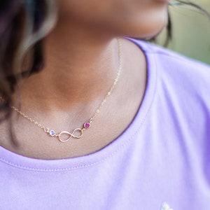May include: A gold infinity necklace with three small gemstones. The gemstones are blue, red, and clear.