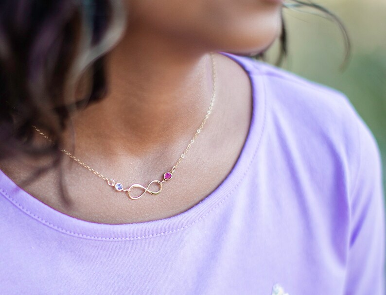 May include: A gold infinity necklace with three small gemstones. The gemstones are blue, red, and clear.