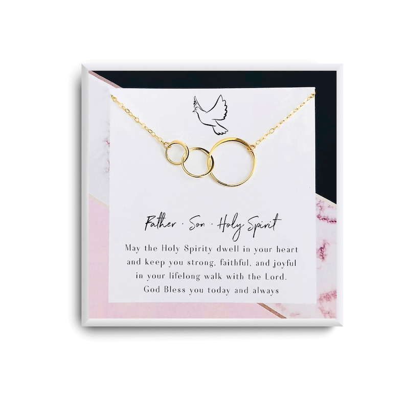 May include: A gold necklace with three interlocking circles and a dove charm. The necklace comes in a white box with a pink marble pattern and a card that reads "Father Son Holy Spirit" and a message about the Holy Spirit.