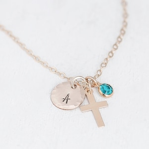 May include: Gold necklace with a small cross charm, a round charm with the letter 'A' engraved on it, and a teal blue gemstone charm.