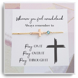 May include: A gold cross charm bracelet with a blue gemstone. The bracelet is on a white background with the text "Whenever you feel overwhelmed Always remember to Pray ON IT Pray OVER IT Pray THROUGH IT".