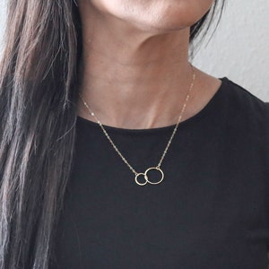 Puede incluir: Un collar de oro con dos c&iacute;rculos entrelazados. El collar est&aacute; puesto por una persona que lleva una blusa negra.