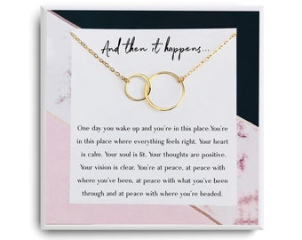May include: A gold necklace with two interlocking circles, presented in a white box with a pink and black marble design. The box includes a card with the text "And then it happens... One day you wake up and you're in this place. You're in this place where everything feels right. Your heart is calm. Your soul is lit. Your thoughts are positive. Your vision is clear. You're at peace, at peace with where you've been, at peace with what you've been through and at peace with where you're headed."
