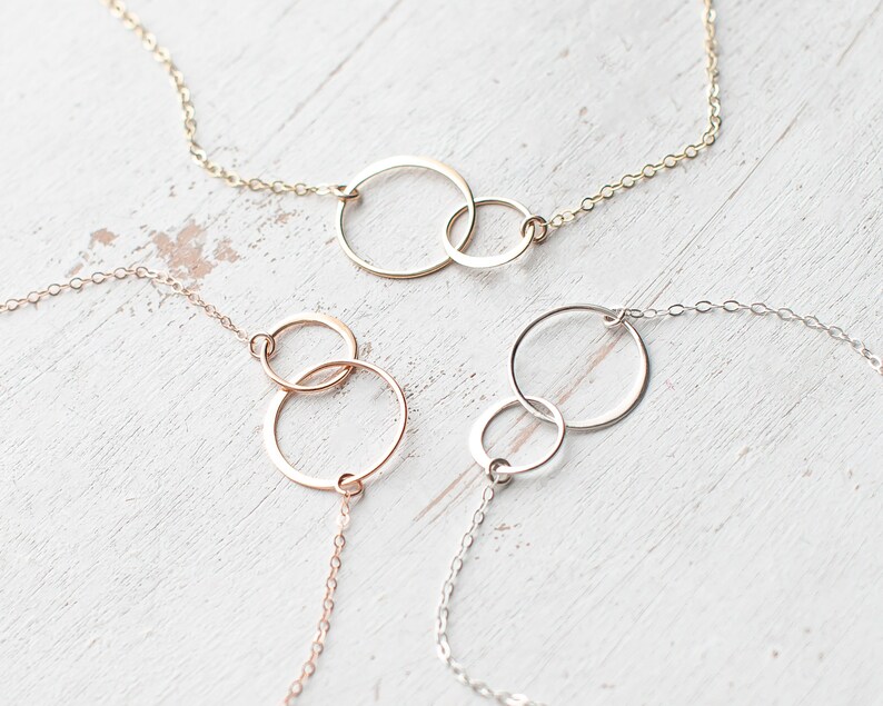 May include: Three delicate necklaces with interlocking circle pendants. The necklaces are made of gold, rose gold, and silver chain.