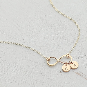 May include: Gold infinity necklace with two small charms, one with the letter 'C' and the other with the letter 'S'.