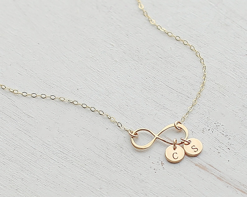 May include: Gold infinity necklace with two small charms, one with the letter 'C' and the other with the letter 'S'.