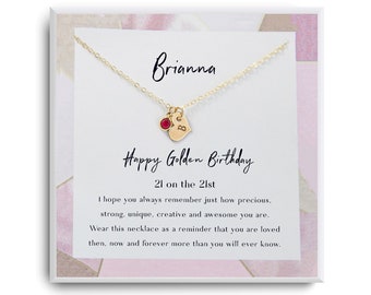 May include: A gold necklace with a heart charm and a red gemstone. The necklace is in a white box with a pink and white floral pattern. The box has the text "Brianna" and "Happy Golden Birthday 21 on the 21st". The box also has a message that says "I hope you always remember just how precious, strong, unique, creative and awesome you are. Wear this necklace as a reminder that you are loved then, now and forever more than you will ever know."