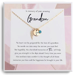 May include: A gold necklace with a small angel wing charm and a letter 'T' charm with a turquoise gemstone. The necklace is displayed in a white box with a pink and white background. The text in the box reads: "In memory of your amazing Grandson. No heart can be prepared for the loss of a grandson. No words can take away the sorrow you must feel. But hopefully, the cherished memories of You will help give you strength in the days ahead. Every time you wear this necklace take comfort in the thought of all those memories you have and the happiness he brought in your life."