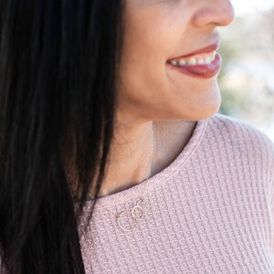 May include: A woman wearing a pink waffle knit sweater with a delicate gold necklace featuring two interlocking circles.