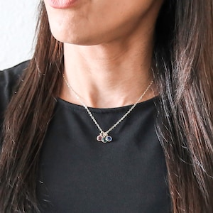 May include: A silver chain necklace with three small charms, each featuring a different colored gemstone. The charms are in a cluster at the center of the necklace.
