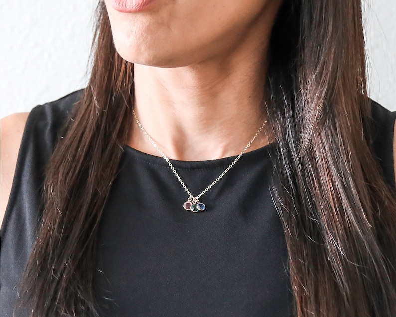 May include: A silver chain necklace with three small charms, each featuring a different colored gemstone. The charms are in a cluster at the center of the necklace.
