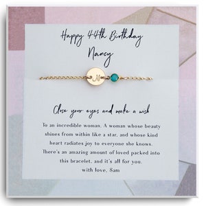 Puede incluir: Un brazalete de oro con un pequeño dije que dice "N" y una piedra turquesa. El brazalete está empaquetado en una caja blanca con un fondo de acuarela rosa y azul. La caja tiene un mensaje que dice "Feliz cumpleaños número 44 Nancy Cierra los ojos y pide un deseo A una mujer increíble. Una mujer cuya belleza brilla desde adentro como una estrella, y cuyo corazón bondadoso irradia alegría a todos los que conoce. Hay una increíble cantidad de amor empaquetado en este brazalete, y es todo para ti. con amor, Sam"