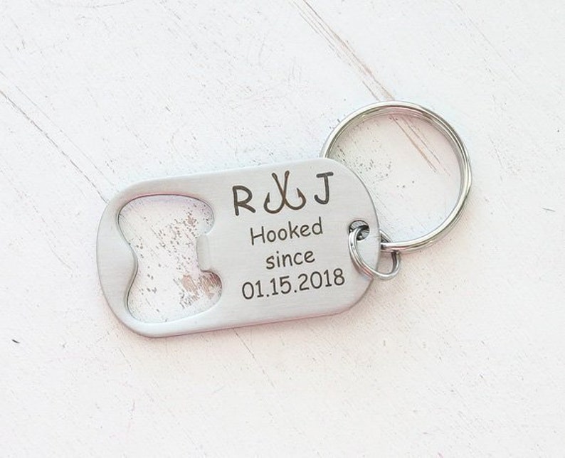 May include: A silver bottle opener keychain with the engraved text "R & J Hooked since 01.15.2018". The keychain has a bottle opener on one end and a keyring on the other.